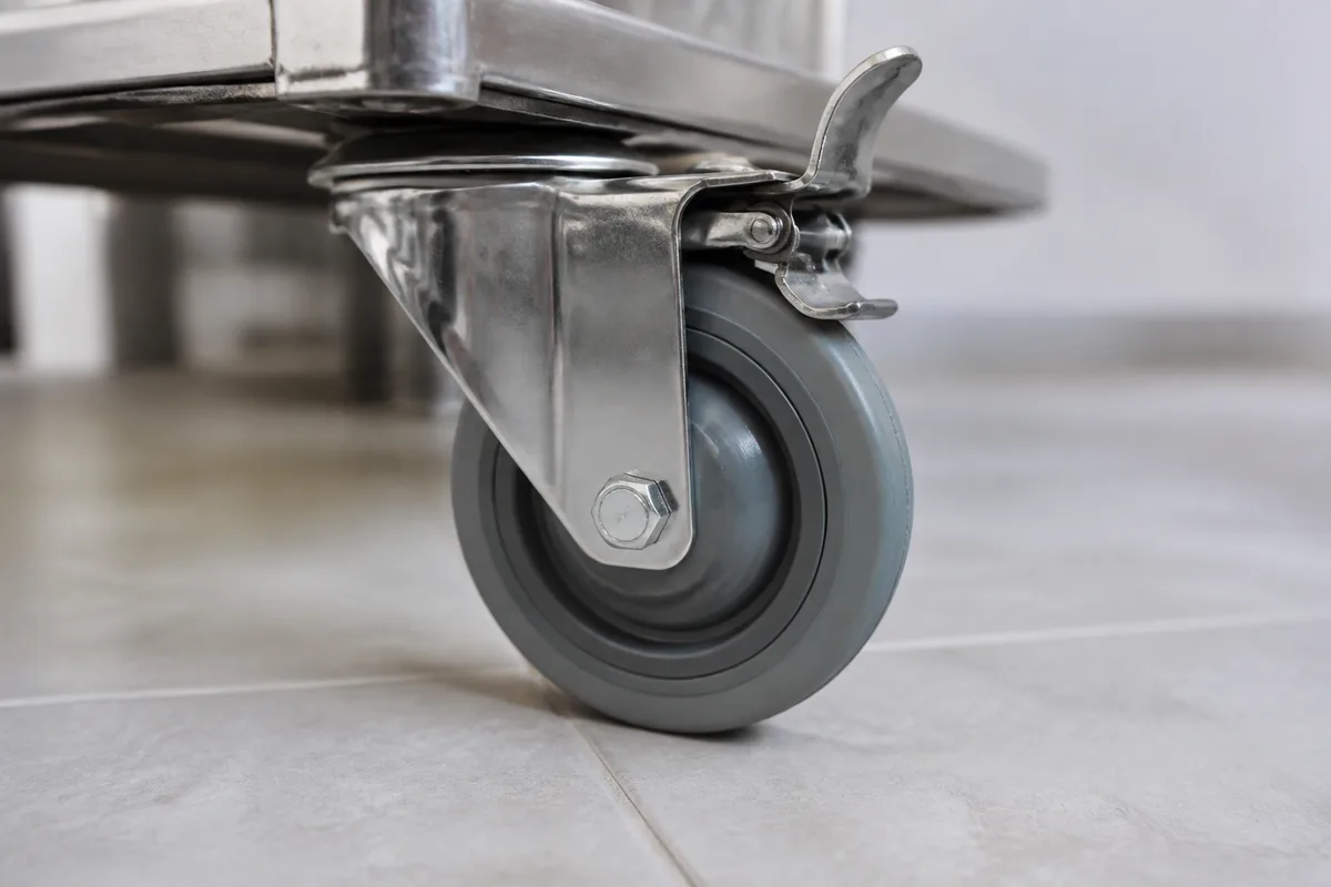 Roue pivotante à bandage caoutchouc gris et frein à pédale sous un plateau de chariot