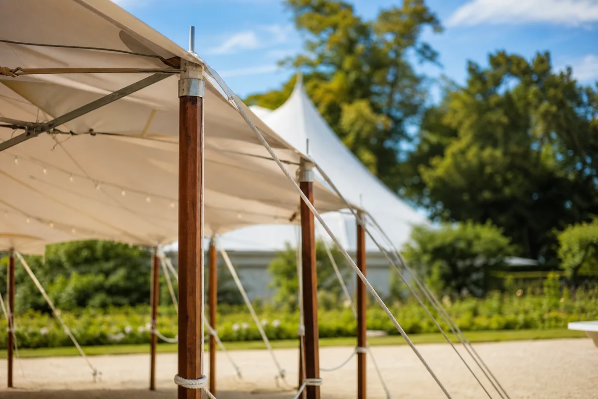 Structure de chapiteau vue de l&rsquo;extérieur avec mâts et cordages tendus dans un grand jardin